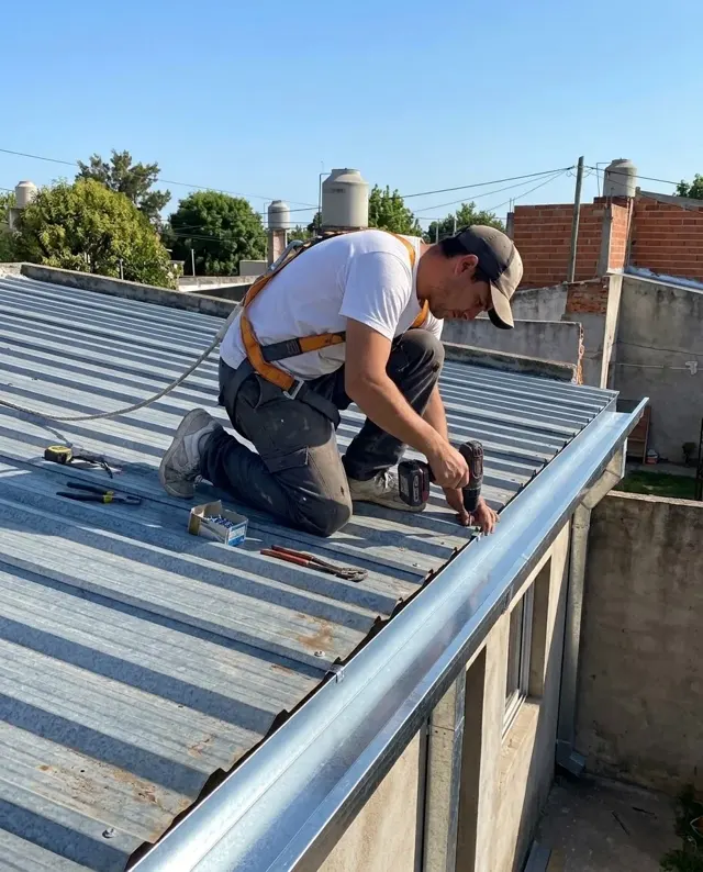 Techista con arnés fijando una canaleta sobre un techo de chapa